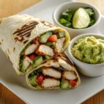 Fresh avocado chicken wrap on a white plate with guacamole and lime wedge,