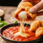 Crispy pizza puffs stacked on a plate with marinara dipping sauce, cheese stretching as one is dipped