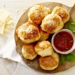 Close-up of golden-brown pizza puffs with marinara sauce and basil garnish on a wooden board