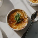 Golden caramelized Crab Brulee Recipe in a white ramekin, garnished with chives and parsley, placed on a marble counter.